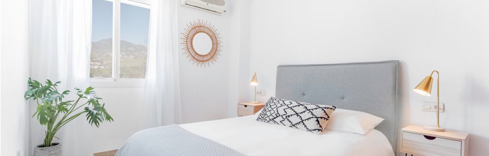 Comfortable Airbnb bedroom with felt headboard with natural fabric cushion, rattan lamp, wood nightstand and a big wooden wardrobe.